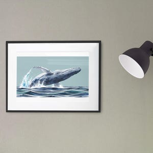 May include: A framed print of a humpback whale breaching out of the water. The whale is gray and white, and the water is a light blue. The print is framed in black.