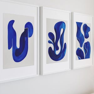 Puede incluir: Tres impresiones artísticas abstractas enmarcadas. Cada impresión presenta un diseño azul único sobre un fondo blanco. La obra de arte se muestra en marcos blancos, creando una estética moderna y minimalista. El arte está colgado en una pared blanca.
