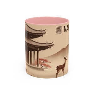 Puede incluir: Taza de cerámica con interior rosa y exterior beige que presenta una escena de pagoda japonesa con un ciervo y la palabra "NARA". El diseño incluye un árbol rojo y una cordillera.