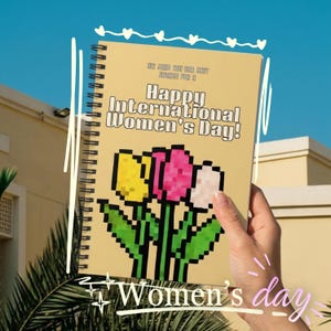 Puede incluir: Un cuaderno con espiral con una cubierta de color amarillo claro. La cubierta presenta el texto "Happy International Women's Day!" y un diseño floral pixelado de tulipanes amarillos, rosas y blancos. El cuaderno se sostiene contra un cielo azul.