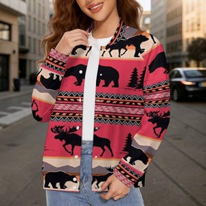 May include: A red bomber jacket with a pattern of black bears, moose, and trees. The jacket has a white collar and button closure. The sleeves and body feature a geometric design in black, white, and tan.