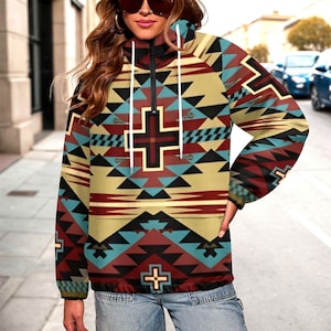 May include: A zip-up hooded jacket with a Southwestern geometric pattern in shades of red, tan, teal, and black. The jacket features a cross design on the front and a high collar with white drawstrings.