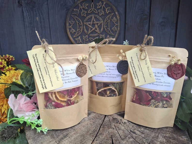 May include: Three light brown kraft paper pouches containing dried botanical ingredients for simmering. Each pouch features a clear window, a tied tag with printed text, a small dried flower sprig, and a decorative wax seal in bronze, black, or red.
