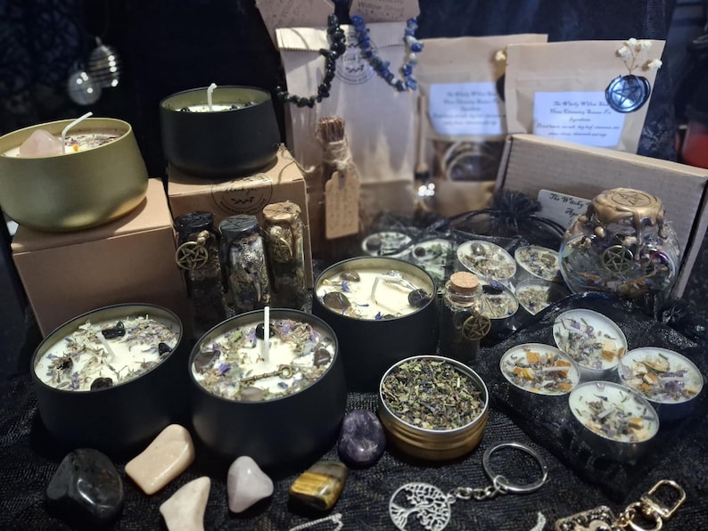 May include: A collection of black and gold metal candle tins filled with wax, dried herbs, and crystals. Includes small glass vials with cork stoppers, tea light candles, a tree of life keychain, and various loose crystals arranged on a dark surface.