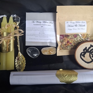 May include: A gift set containing two yellow beeswax candles tied with twine and dried flowers, a gold-toned decorative spoon, two polished crystals, a packet of dried herbs labelled The Witchy Willow Shed, a wood slice with black ink, and a scroll with a gold seal.