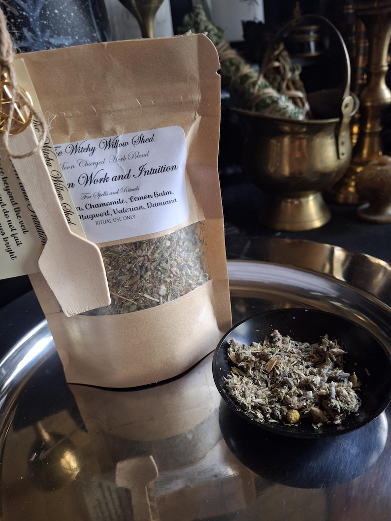 May include: A brown paper pouch labeled Witchy Willow Shed Moon Charged Herb Blend for Dream Work and Intuition, containing dried herbs including chamomile, lemon balm, mugwort, valerian, and damiana. A small wooden scoop is attached to the front.