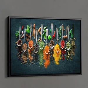 May include: A black framed canvas print featuring a culinary still life. Silver spoons are arranged across the top, each holding a different spice or herb. Vibrant colors of red, green, yellow, and brown spices are scattered below.