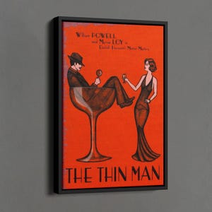 Könnte beinhalten: Ein schwarzer gerahmter Leinwanddruck eines Vintage-Filmplakats für "The Thin Man" mit William Powell und Myrna Loy. Das Plakat zeigt eine stilisierte Illustration eines Mannes und einer Frau, die in einem Martini-Glas sitzen und beide ein Glas Wein halten.