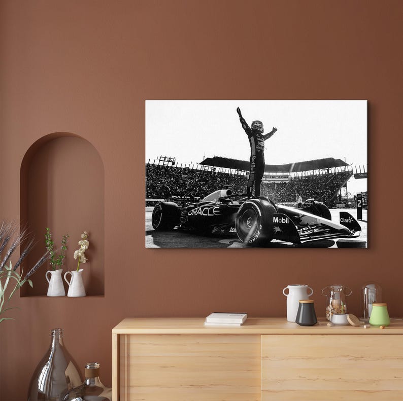 May include: Black and white photograph of a Formula 1 race car with the Oracle logo. A driver stands on top of the car with arms raised in victory. The background shows a stadium filled with spectators.