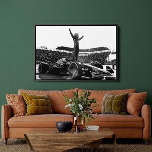 May include: Black and white framed print of a Formula 1 race car with a driver standing on top, arms raised in victory. The car has sponsor logos including "Oracle" and "Mobil". The background shows a stadium filled with spectators.