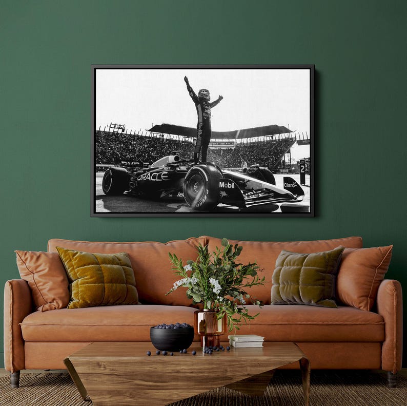 May include: Black and white framed print of a Formula 1 race car with a driver standing on top, arms raised in victory. The car has sponsor logos including "Oracle" and "Mobil". The background shows a stadium filled with spectators.