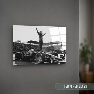 May include: Black and white print of a Formula 1 race car with a driver standing on top, arms raised in victory. The car has sponsor logos including "Oracle" and "Mobil." The image is displayed on a wall with the text "TEMPERED GLASS" at the bottom.