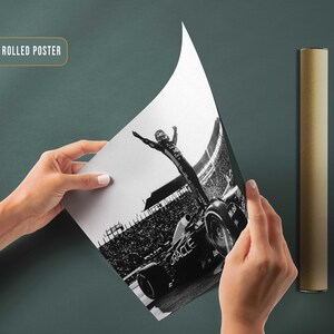 May include: A black and white canvas rolled poster featuring a Formula 1 race car and a driver celebrating a victory. The poster is being held up, revealing the image, with a rolled poster tube beside it. The text "CANVAS ROLLED POSTER" is visible.