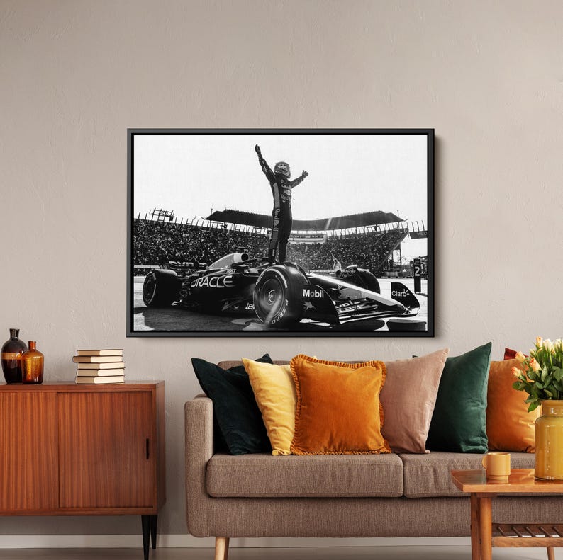 May include: Black and white framed print of a Formula 1 race car with a driver standing on top, arms raised in victory. The car has sponsor logos, and the background shows a stadium filled with spectators.