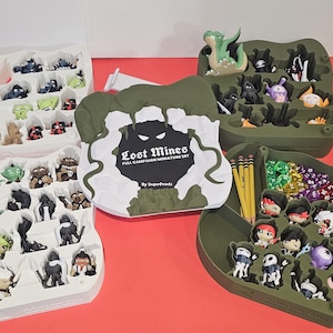 May include: A Lost Mines full campaign miniature set featuring two white and two olive green molded plastic trays. The trays contain various small painted character figurines, a collection of multi-colored polyhedral dice, and yellow pencils.