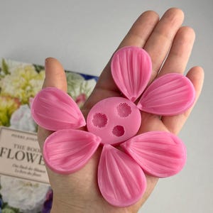 以下が含まれることがあります： 花びらを作るためのピンクのシリコンモールド。モールドは5つの花びらの形と、3つの小さな円がある中央部分を持っています。