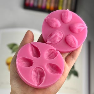 Puede incluir: Dos moldes de silicona rosa con cinco impresiones en forma de pétalo cada uno. Los moldes están diseñados para crear decoraciones con forma de flor.