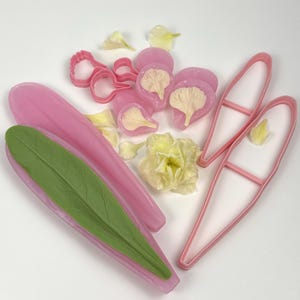 May include: A collection of pink and green silicone molds and cutters for crafting. The image shows a variety of shapes, including leaf and petal molds, along with pink cutters and yellow flower petals. Ideal for creating floral decorations.