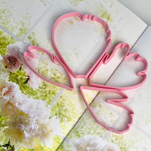 May include: Three pink plastic cookie cutters shaped like flower petals. The cutters feature distinct, organic outlines with curved edges and varying sizes, designed for cutting dough into specific floral shapes for baking and crafting projects.