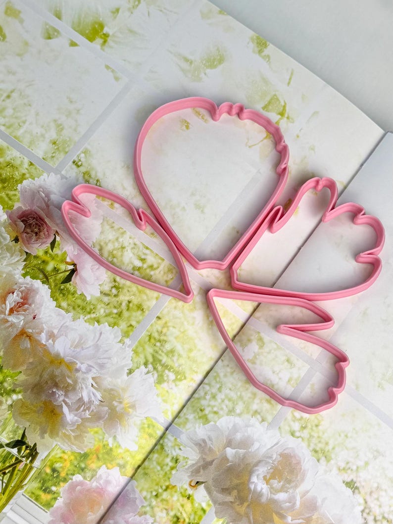 May include: Three pink plastic cookie cutters shaped like flower petals. The cutters feature distinct, organic outlines with curved edges and varying sizes, designed for cutting dough into specific floral shapes for baking and crafting projects.
