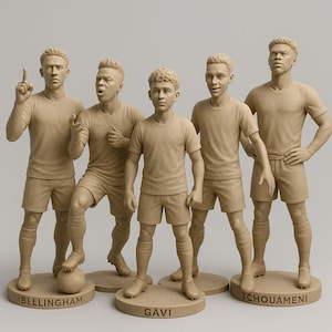 Può includere: Cinque statuette di calciatori beige in abbigliamento sportivo, ciascuna su una base circolare con un nome. Le statuette sono in varie pose d'azione. I nomi Bellingham, Gavi e Tchouameni sono visibili.
