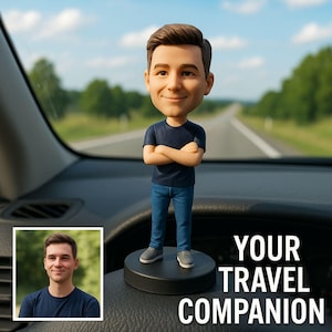 May include: A bobblehead figurine of a man with crossed arms, wearing a navy blue t-shirt and jeans, standing on a black base. The text "YOUR TRAVEL COMPANION" is displayed. The background shows a road and a blue sky.