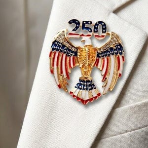 Large 2.5-inch gold-tone patriotic eagle brooch with red and white enamel wings and '250' star-patterned crest, shown to scale for the 2026 American Semi quincentennial.