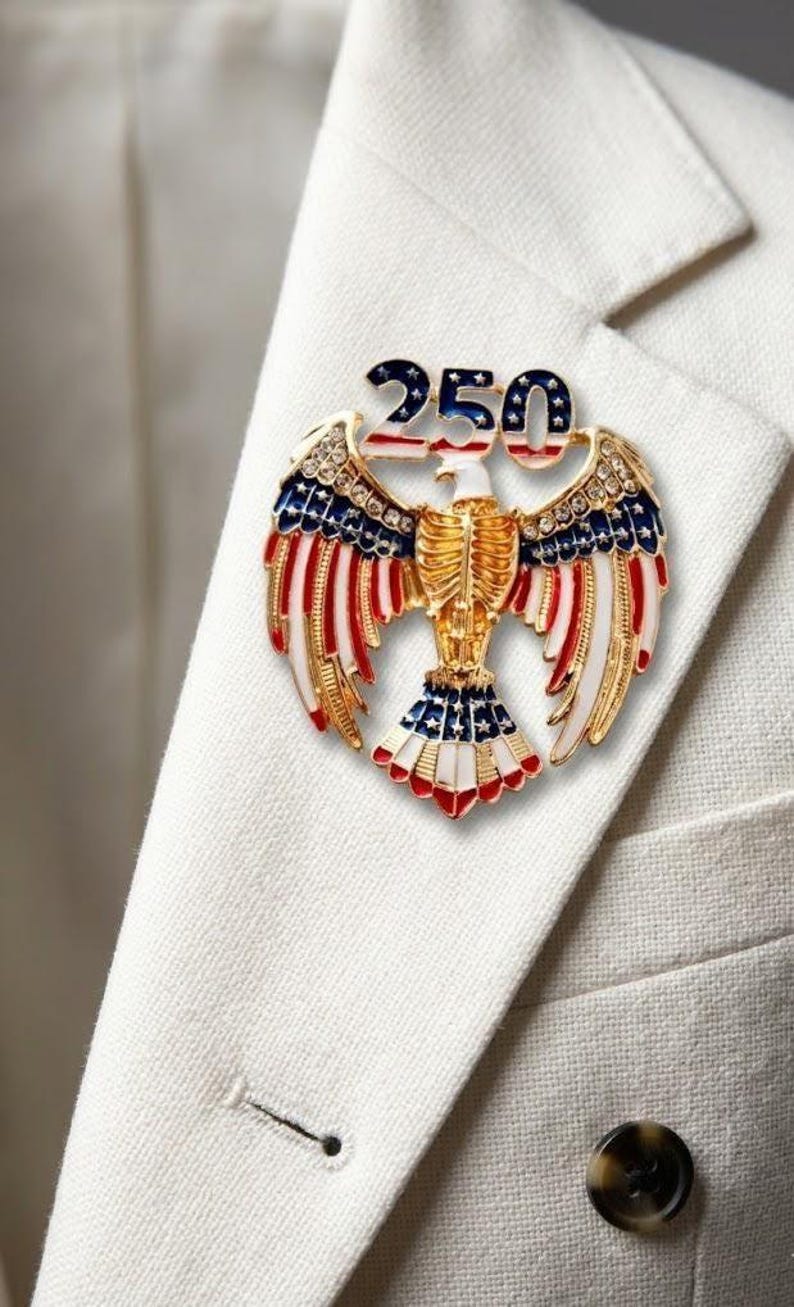 Large 2.5-inch gold-tone patriotic eagle brooch with red and white enamel wings and '250' star-patterned crest, shown to scale for the 2026 American Semi quincentennial.
