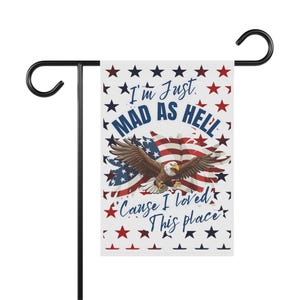 Op de afbeelding: Een rechthoekige tuinvlag met een witte achtergrond en een patroon van rode en blauwe sterren. In het midden staat een Amerikaanse zeearend afgebeeld voor een wapperende Amerikaanse vlag. De tekst luidt: I'm Just MAD AS HELL 'Cause I loved This place.