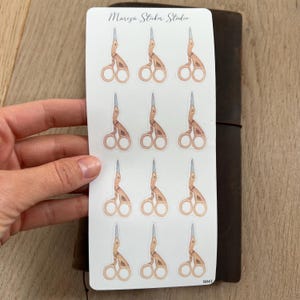 Può includere: Un foglio di 12 adesivi di forbici dorate su sfondo bianco. Gli adesivi sono disposti in quattro file di tre. Il testo "Marza Sticker Studio" e "S041" è stampato sul foglio.