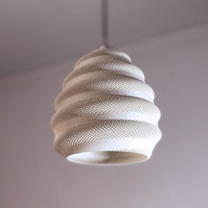 Puede incluir: Una lámpara colgante blanca y texturizada con un diseño en espiral. La lámpara está suspendida del techo y tiene una base ancha y abierta. La superficie de la lámpara está cubierta de pequeños puntos espaciados uniformemente.