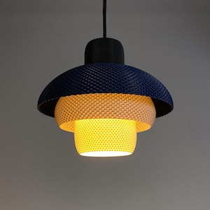 Könnte beinhalten: Eine moderne Pendelleuchte mit einem strukturierten, geschichteten Design. Der obere Schirm ist marineblau, der mittlere Abschnitt hellorange und der untere Teil leuchtend gelb. Sie hängt an einem schwarzen Kabel.
