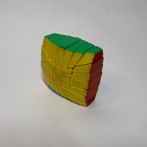 May include: A colorful puzzle toy with a unique shape. The puzzle features green, yellow, and red sections. The toy is designed with multiple interlocking pieces, creating a complex and engaging challenge. The overall design is geometric and visually appealing.