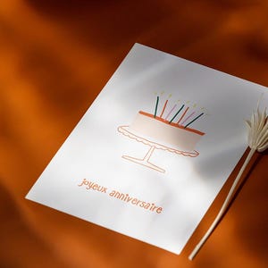 Carte Joyeux Anniversaire avec un gros gâteau d'anniversaire dessiné dessus, dans les tons jaunes orangés.