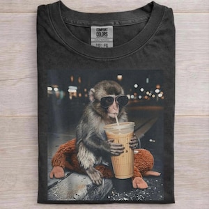 May include: A white ceramic mug with a black handle and the text "But First, Coffee" in a bold, black font. The mug is set against a neutral background, highlighting its simple design.