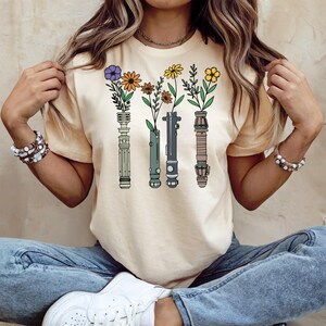 A woman wearing a t-shirt with a graphic design of four colorful flowers and plants, along with a necklace.