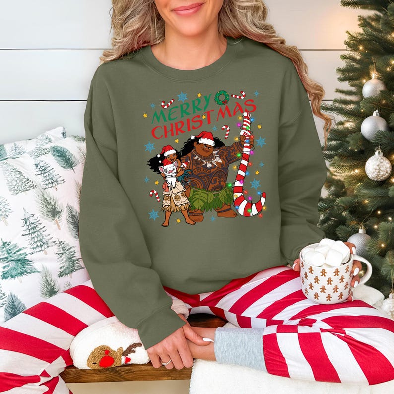 A woman wearing a green sweatshirt with a Christmas-themed graphic and holding a mug of hot chocolate.