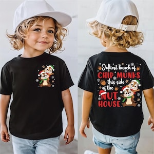 Peut inclure: T-shirt noir à manches courtes avec un motif de Noël de deux tamias portant des bonnets et des écharpes de Père Noël. Le dos du t-shirt porte l'inscription "Jolliest bunch of Chipmunks this side of the Nut House."