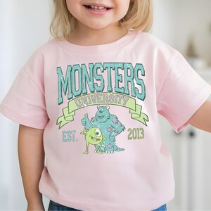 A young girl wearing a pink t-shirt with a graphic design featuring a character from the animated movie Monsters University.