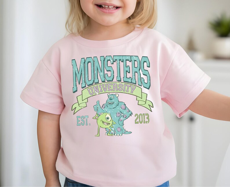 A young girl wearing a pink t-shirt with a graphic design featuring a character from the animated movie Monsters University.