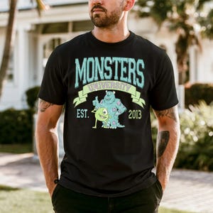 A man wearing a black t-shirt with a graphic design featuring a character from the animated movie Monsters University.