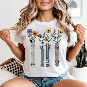 A woman wearing a white t-shirt with a graphic design of four vases with flowers and plants.
