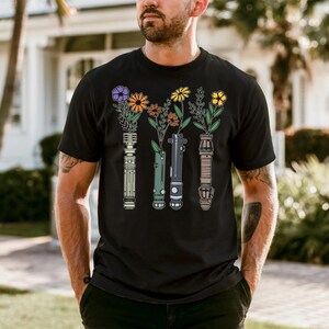 A man wearing a black t-shirt with a graphic design of colorful flowers and vases.