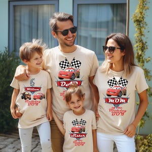 A family of four, consisting of a father, mother, and two children, are posing together in front of a building. They are all wearing matching t-shirts with a design featuring a red car and checkered flags.
