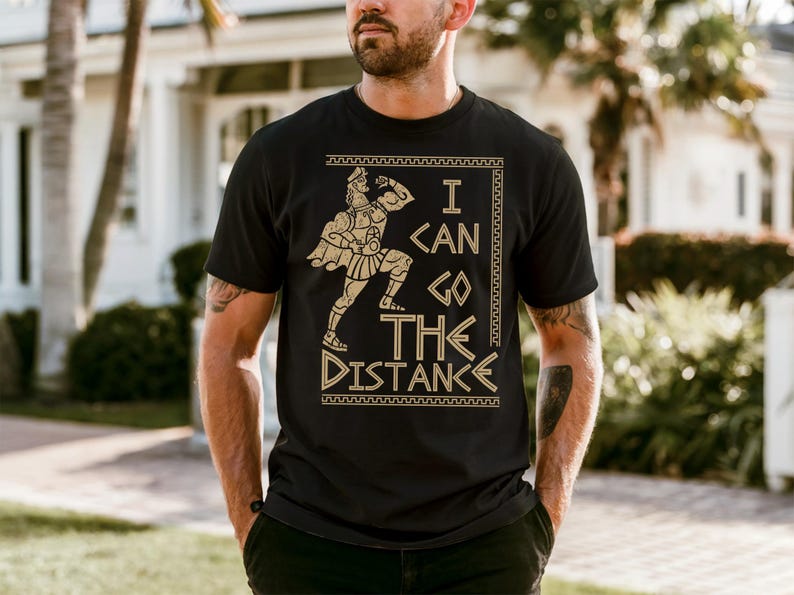 A man wearing a black t-shirt with a graphic design printed on it, standing in front of a house.