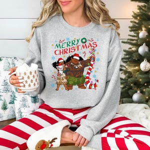 A woman wearing a gray sweatshirt with a Christmas-themed graphic and holding a mug of hot chocolate.