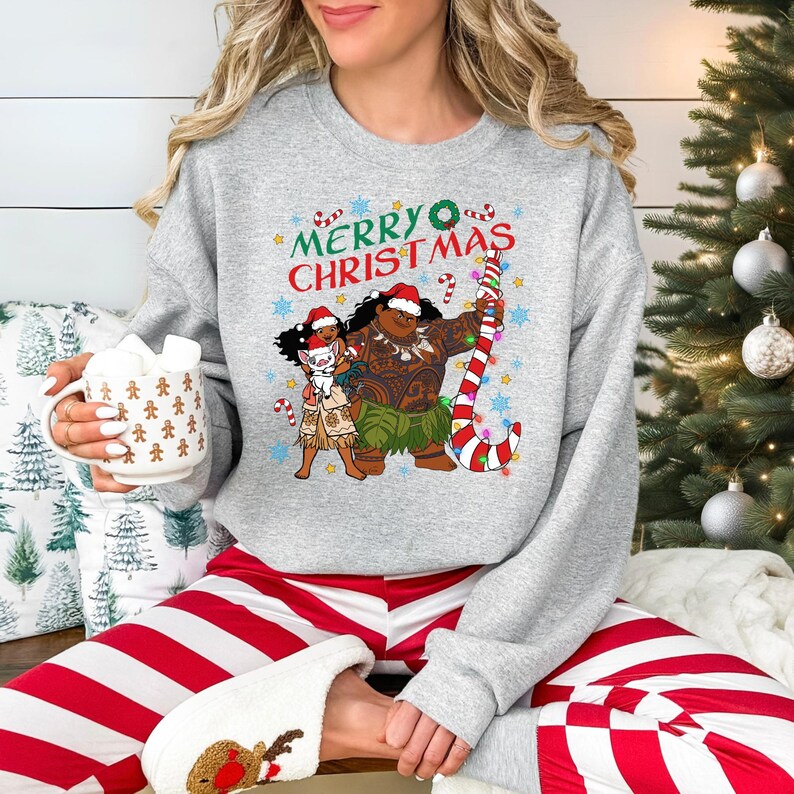 A woman wearing a gray sweatshirt with a Christmas-themed graphic and holding a mug of hot chocolate.