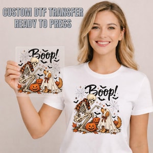 May include: A white t-shirt and a square DTF transfer sheet featuring a graphic of a skeleton touching the nose of a dog wearing a ghost costume. The design includes the text Boop!, orange pumpkins, black bats, and spider webs on both items.