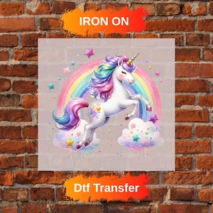 Peut inclure: Transfert DTF coloré avec une licorne aux crins et à la queue arc-en-ciel, une corne dorée et un arc-en-ciel en arrière-plan. L'inscription "Iron On" est visible en haut.