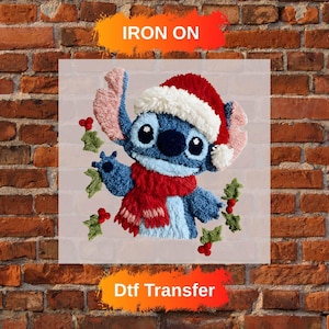 May include: A blue character wearing a Santa hat and red scarf, holding holly. The image is a DTF transfer with the words "Iron On" and "Dtf Transfer" in orange and white text.